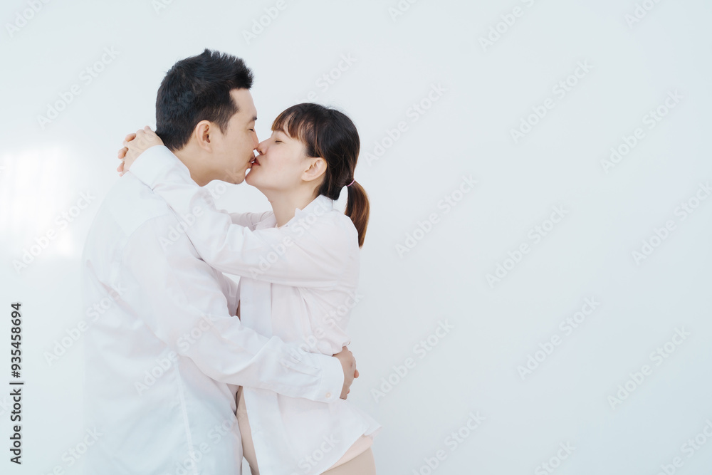 A happy Asian couple, expecting a baby, embraces in a cozy living room. The pregnant woman smiles warmly, while the man lovingly supports her, capturing a moment of joyful anticipation. A happy Asian couple, expecting a baby, embraces in a cozy living room. The pregnant woman smiles warmly, while the man lovingly supports her, capturing a moment of joyful anticipation.