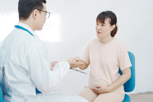 Asian female doctor listens to belly of pregnant mother during a prenatal exam in clinic. doctor provides caring advice, ensuring the health and happiness of the expecting mother and baby.