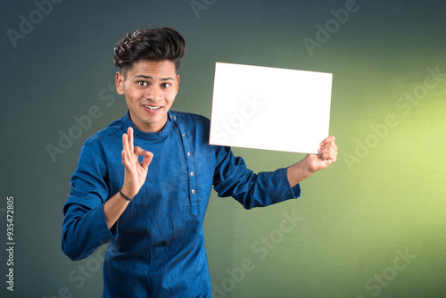 A happy young man is holding and displaying a signboard or placard on a dark background.