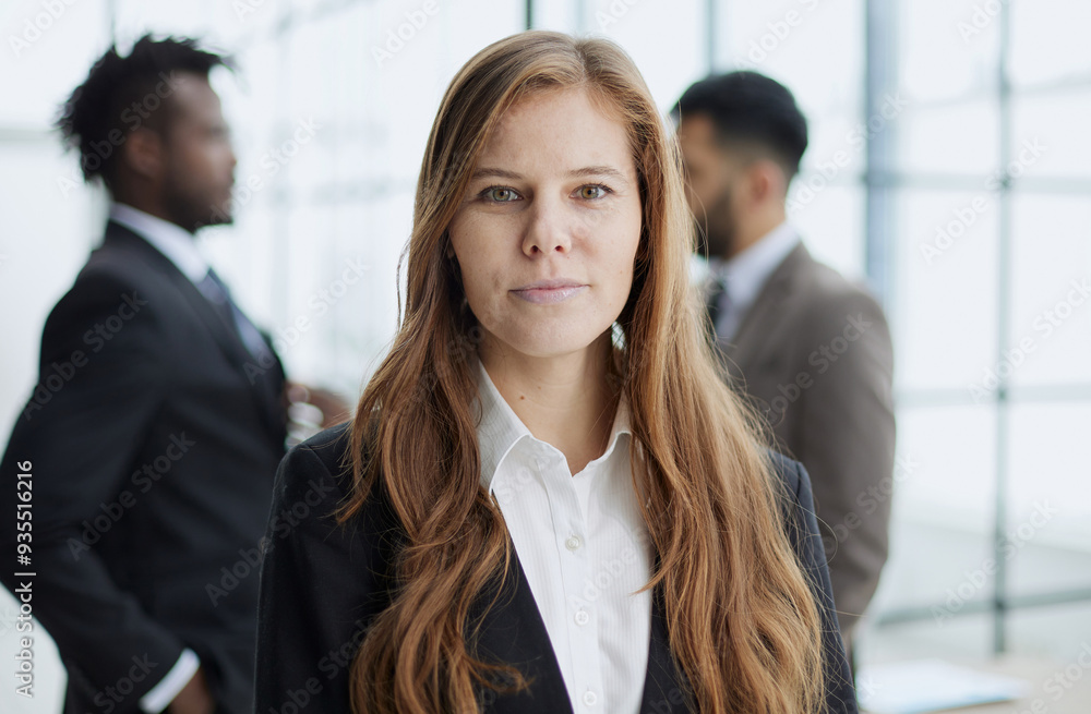 A beautiful business woman stands and looks confidently into the camera against the background of her colleagues