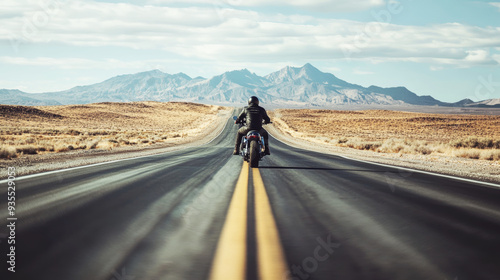 Motorcyclist rides down a long, empty road in a desert landscape with mountains in the distance. The image captures a sense of freedom and adventure on an open highway. photo