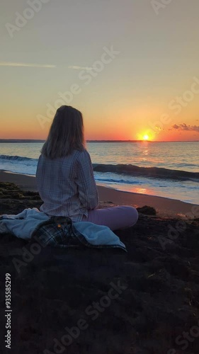 A person sitting on a sandy beach, meditating and deeply immersed in thought against the backdrop of sunrise. The sun rises over the sea, offering a serene view of the ocean and beach.