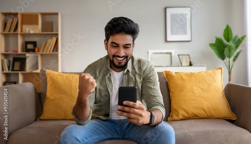 Young indian man sitting on sofa at home and looking at mobile phone screen