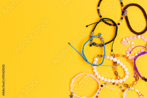 Various handmade bracelets made of beads and cords scattered on a yellow background. Place for text.