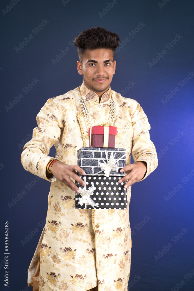 Young happy smiling handsome man holding gift box and posing on dark background Young happy smiling handsome man holding gift box and posing on dark background