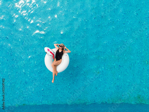 Beach vacation woman relaxing in pool float unicorn inflatable ring floating on turquoise pool water. Aerial top view from drone