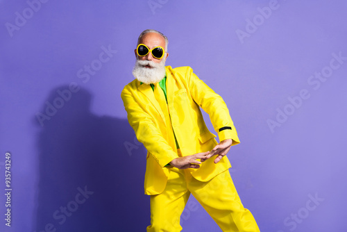 Portrait of funny extravagant aged man enjoy dancing yellow suit isolated on purple color background photo