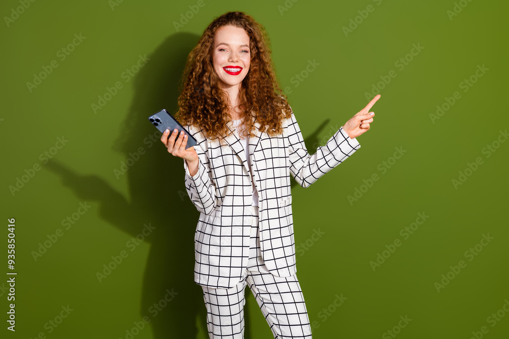 Photo portrait of lovely young lady hold device point empty space dressed stylish white plaid garment isolated on khaki color background Photo portrait of lovely young lady hold device point empty space dressed stylish white plaid garment isolated on khaki color background