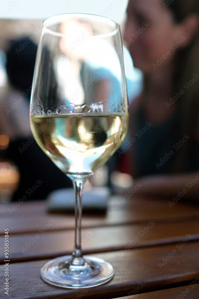 Wineglass with white wine and a blurred person in the background Wineglass with white wine and a blurred person in the background