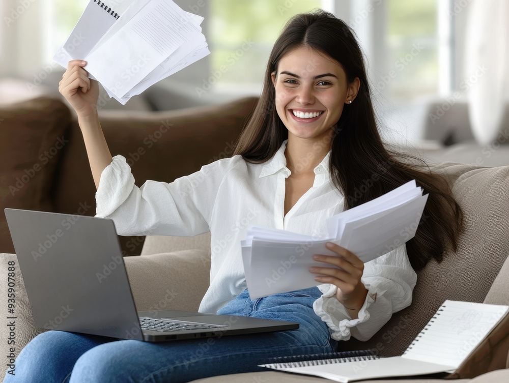 Excited young woman celebrating success while working from home with laptop and papers Excited young woman celebrating success while working from home with laptop and papers