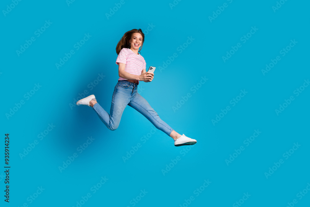 Full size photo of pretty young girl running hold device wear trendy pink striped outfit isolated on blue color background Full size photo of pretty young girl running hold device wear trendy pink striped outfit isolated on blue color background