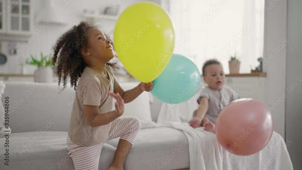 Little siblings playing, African American children throwing balloons at home. Family and childhood concept, active game in children party, black girl with curly hair hitting balloon, joy and happiness Little siblings playing, African American children throwing balloons at home. Family and childhood concept, active game in children party, black girl with curly hair hitting balloon, joy and happiness