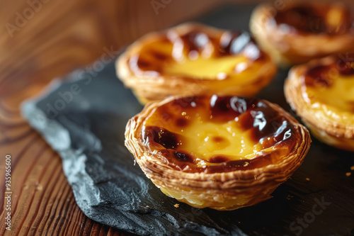 Portuguese pastel de nata on a slate plate is lit by natural light against a wood table backdrop. photo