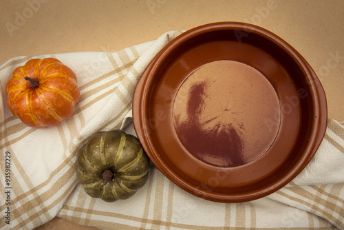 top view of an empty earthen plate with autumn decorative pumpkins on a brown table.autumn food background