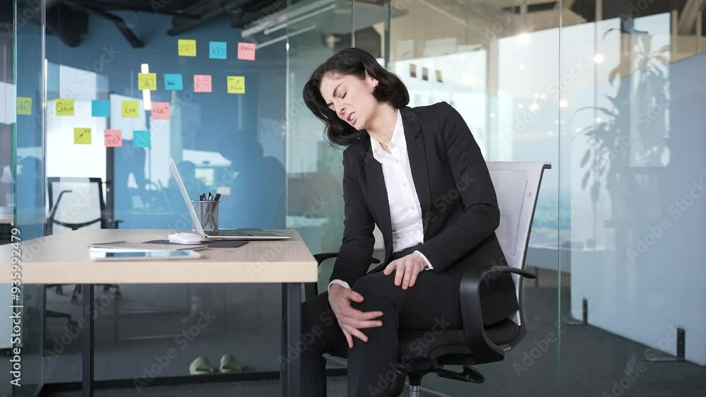Businesswoman sitting in office feeling discomfort from knee pain. Workplace health and wellness with emphasis on need for proper ergonomic setup to alleviate joint stress in professional environments Businesswoman sitting in office feeling discomfort from knee pain. Workplace health and wellness with emphasis on need for proper ergonomic setup to alleviate joint stress in professional environments