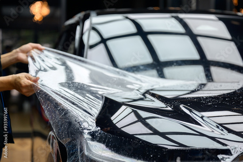 A worker is applying transparent film to a car to protect it from gravel and scratches on the hood of a black car. Applying transparent paint protection film photo