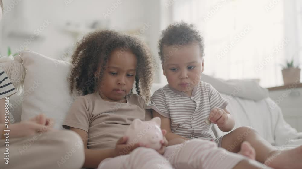 Cute funny African girl holding piggy bank, siblings and friends putting coins. Children playing with money box, learning to save pocket money, financial and economy education for kids, portrait Cute funny African girl holding piggy bank, siblings and friends putting coins. Children playing with money box, learning to save pocket money, financial and economy education for kids, portrait