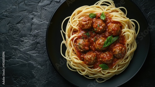 Spaghetti in savory Bolognese sauce with meatballs, served on a black plate, with a textured dark table background, top view.