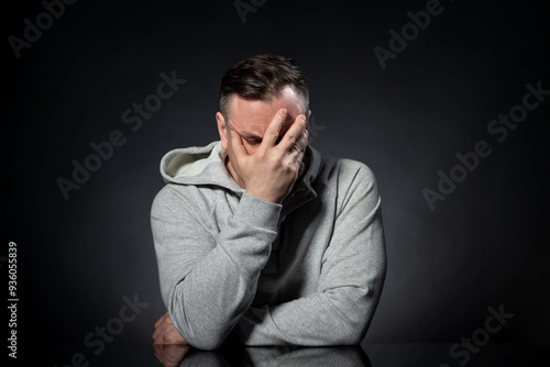 Photography A man in a white hoodie sits at a table and makes a facepalm, on a black background