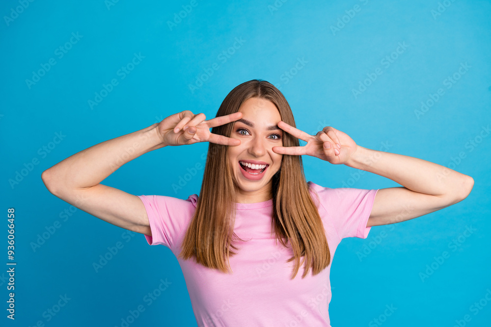 Photo portrait of pretty young girl excited show v-sign wear trendy pink outfit isolated on blue color background Photo portrait of pretty young girl excited show v-sign wear trendy pink outfit isolated on blue color background