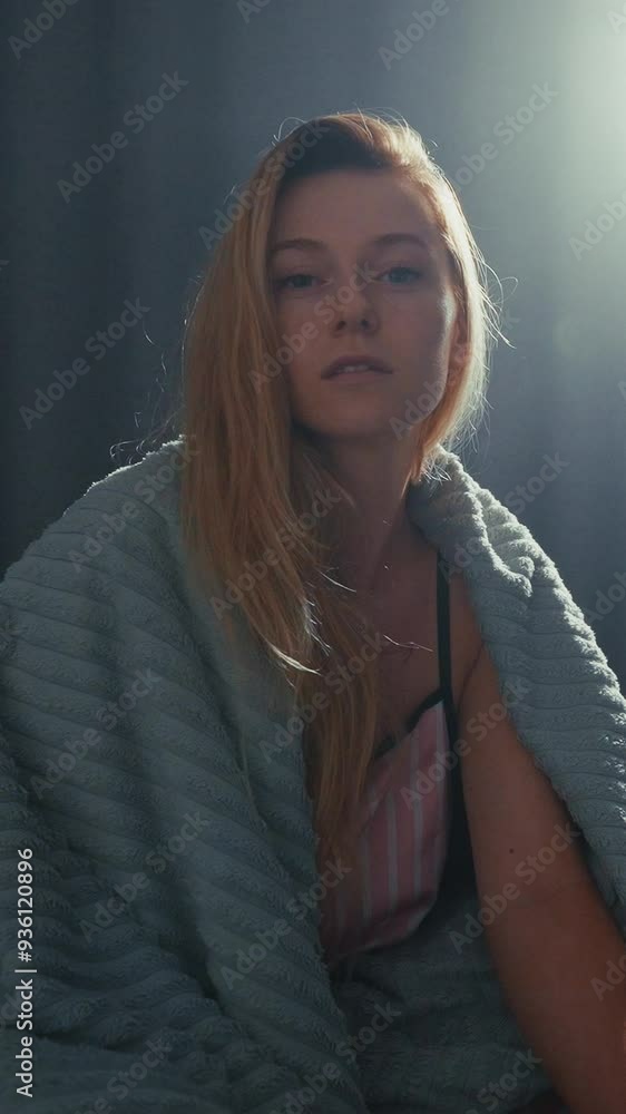Woman sitting on bed wrapped in blanket during early morning light Woman sitting on bed wrapped in blanket during early morning light