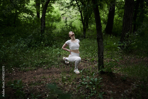 Young caucasian woman in white sportswear exercising in green forest park