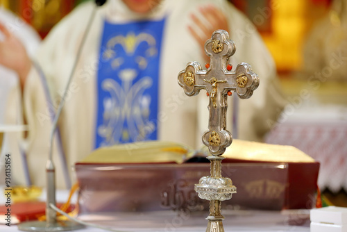 Fotografi Holy Cross with Jesus Christ on the altar during the Holy Mass, the priest in the background and empty space for text
