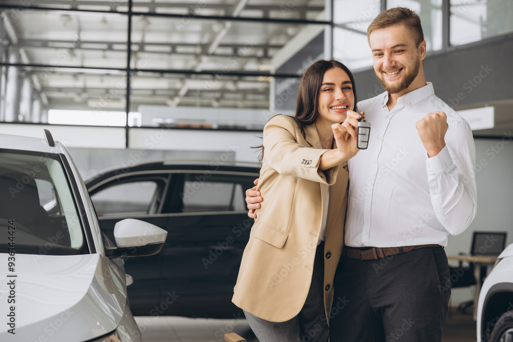 Happy young couple in casual clothes hugging and showing keys to new car in car showroom Happy young couple in casual clothes hugging and showing keys to new car in car showroom