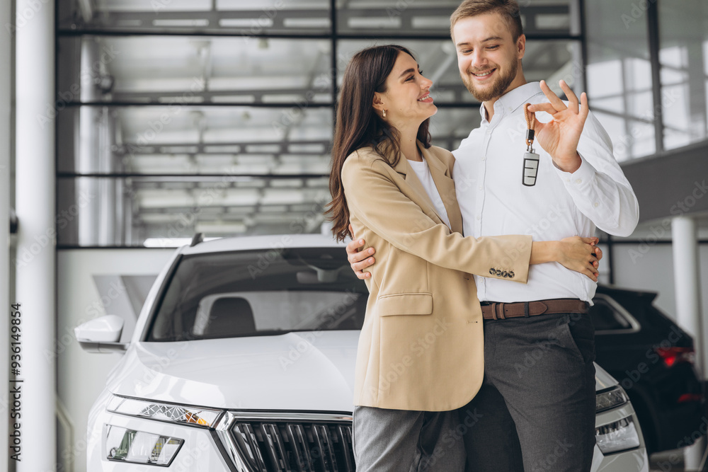 Happy young couple in casual clothes hugging and showing keys to new car in car showroom Happy young couple in casual clothes hugging and showing keys to new car in car showroom