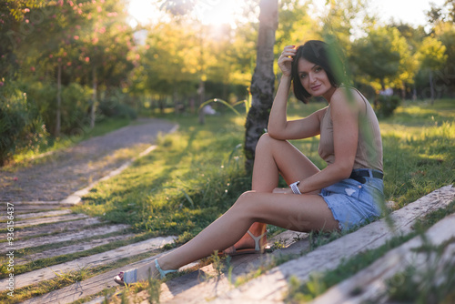 Portrait of a young pretty woman, sitting on a wooden stairs in green public park 