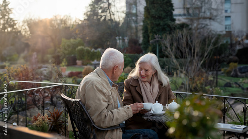 An elderly couple enjoys tea together in a beautiful garden, sharing a peaceful moment and conversation, symbolizing love, companionship, and the beauty of aging.