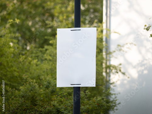 Empty election poster mockup. Template for an ad placard at a street mounted to a lamp post. Blank advertisement space in front of green leaves.
