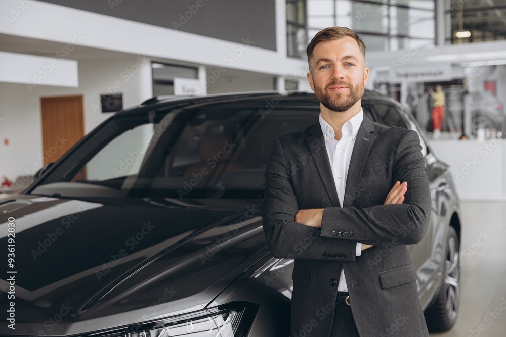 Portrait of a handsome young male car salesman working on the showroom floor. Happy salesperson standing in a car showroom Portrait of a handsome young male car salesman working on the showroom floor. Happy salesperson standing in a car showroom