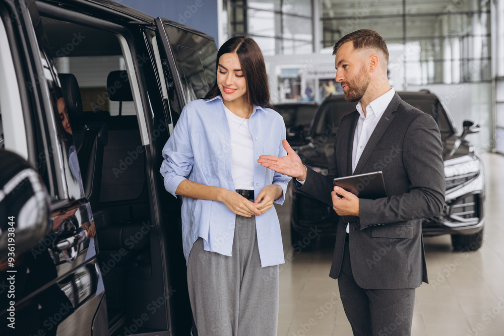 Car Sales Manager Showing Auto Minivan To Caucasian Lady Buyer Standing In Luxury Automobile Dealership Store. Buying Vehicle Concept Car Sales Manager Showing Auto Minivan To Caucasian Lady Buyer Standing In Luxury Automobile Dealership Store. Buying Vehicle Concept