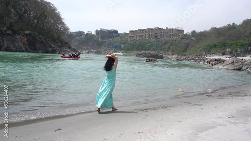 A girl in a blue dress walks on the beach near the Ganges. Rishikesh, India.