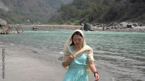 A girl in a blue dress walks on the beach near the Ganges. Rishikesh, India.