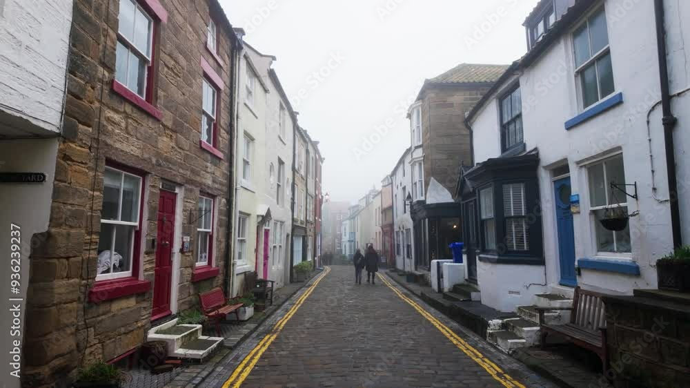 People walking along the quite streets of Staithes a sleepy fishing village on the Yorkshire coast of England. With cobbled streets and old stone built houses. Harbor walls and friendly public houses. People walking along the quite streets of Staithes a sleepy fishing village on the Yorkshire coast of England. With cobbled streets and old stone built houses. Harbor walls and friendly public houses.