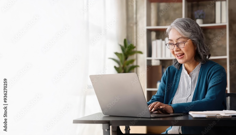 An elderly woman smiles while working on her laptop at home, surrounded by natural light and greenery. An elderly woman smiles while working on her laptop at home, surrounded by natural light and greenery.