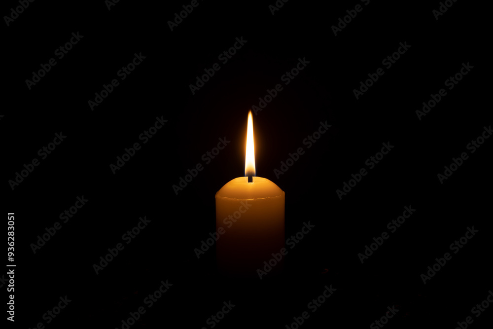 A single candle light glowing on a big white candle on table in church for Christmas, funeral or memorial service with copy space isolated on black background A single candle light glowing on a big white candle on table in church for Christmas, funeral or memorial service with copy space isolated on black background
