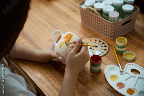 Cuadro en lienzo Top view of woman painting with brush on clay pottery mug in workshop