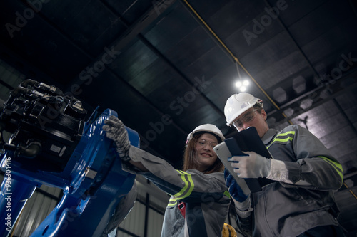 Engineer with helmet safety standing by robotic arm and operating machine in industry factory, technician worker check for repair maintenance electronic operation