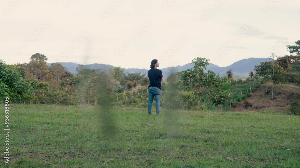 Man stands alone in a lush meadow surrounded by hills and trees in Medellín, Antioquia, capturing a moment of solitude and natural beauty. Man stands alone in a lush meadow surrounded by hills and trees in Medellín, Antioquia, capturing a moment of solitude and natural beauty.