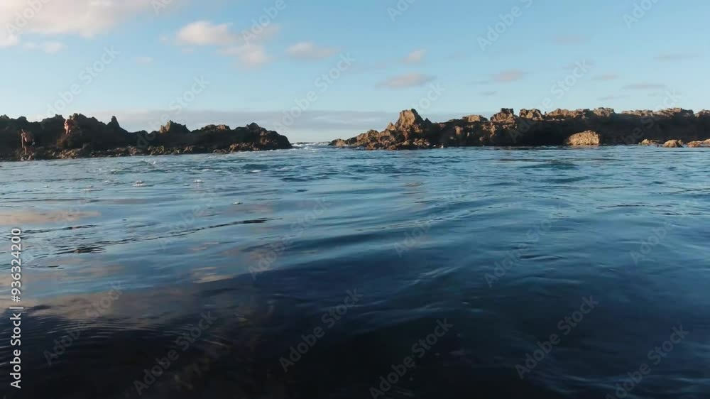 A tranquil scene of calm coastal waters as the sun sets behind rocky cliffs, casting a warm glow over the ocean and sky. A tranquil scene of calm coastal waters as the sun sets behind rocky cliffs, casting a warm glow over the ocean and sky.