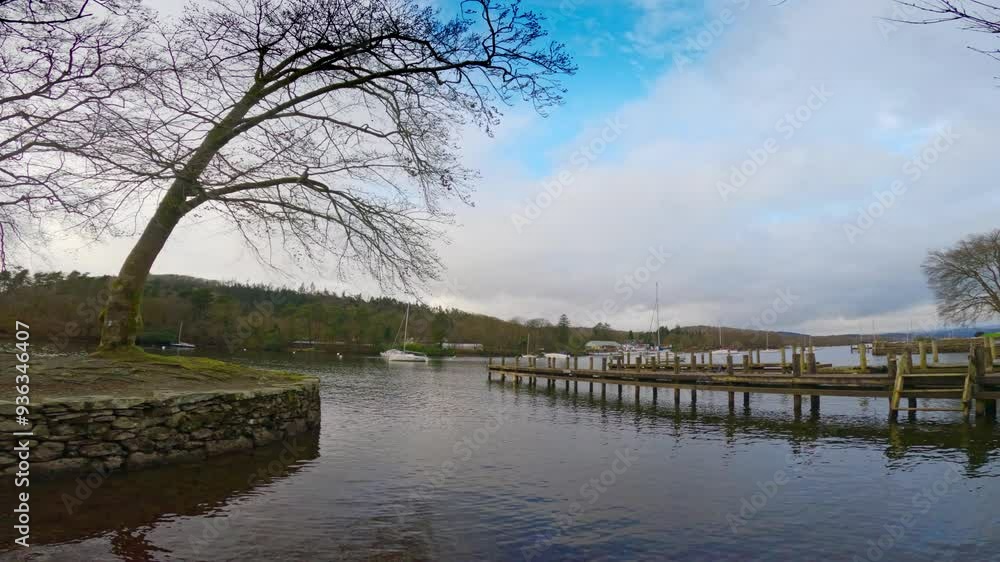Lake Windermere in the English Lake District, with its iconic wooden jetty, historic stone-built buildings, and moody grey skies Lake Windermere in the English Lake District, with its iconic wooden jetty, historic stone-built buildings, and moody grey skies