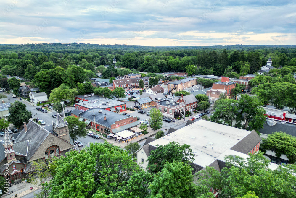 Obraz premium aerial view of rhinebeck new york (hudson valley small town next to catskill mountains) trees main street homes businesses houses (residential and commercial downtown area) drone looking down sunset
