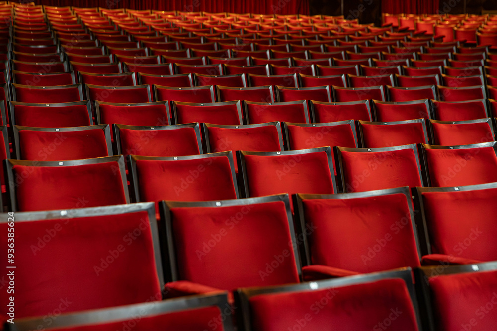 Several red theater seats, with symmetrical framing between the chairs. Several red theater seats, with symmetrical framing between the chairs.