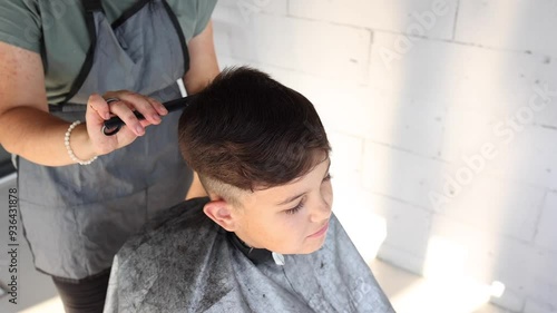 A man is cutting a boy's hair. The boy is sitting on a chair while the man is cutting his hair