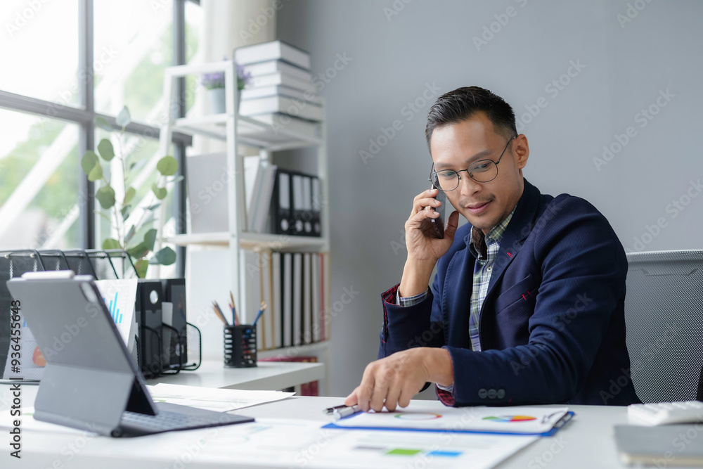 Businessman is working in his office, analyzing charts and talking on the phone about the company's performance Businessman is working in his office, analyzing charts and talking on the phone about the company's performance