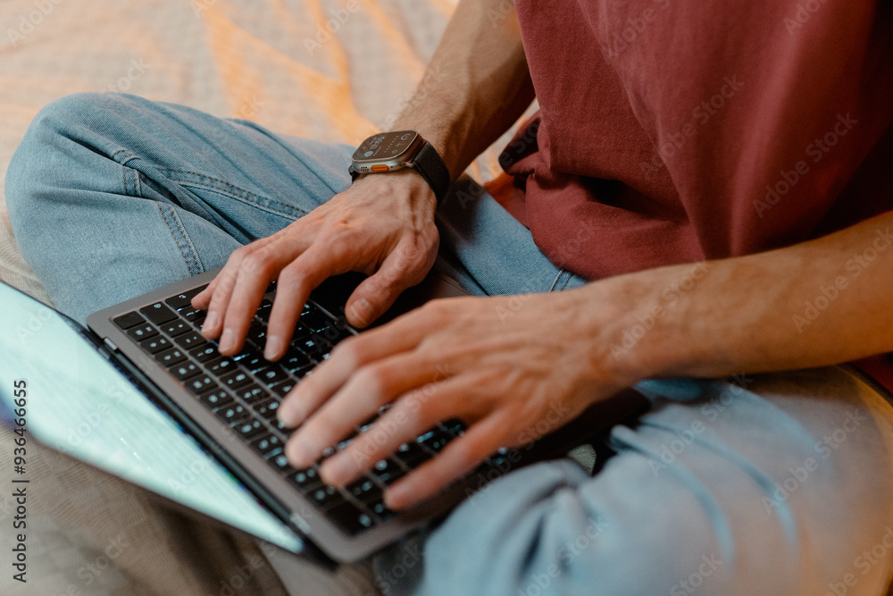 A man is typing on a laptop while sitting on a bed at home. Close-up of his hands, an unrecognizable person A man is typing on a laptop while sitting on a bed at home. Close-up of his hands, an unrecognizable person