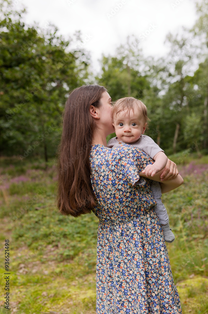Portrait of a young mother in a summer dress with a baby son in her arms in the garden or park. happy family concept. A cute baby is smiling at the camera Portrait of a young mother in a summer dress with a baby son in her arms in the garden or park. happy family concept. A cute baby is smiling at the camera